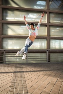 A joyful dancer in a colorful cropped top and jeans leaps gracefully, wearing headphones and