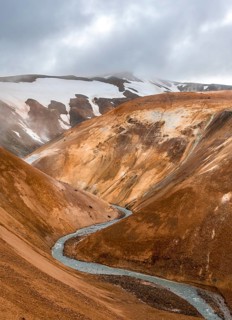 Steaming stream between colourful rhyolite mountains and snowfields, Hveradalir geothermal area,