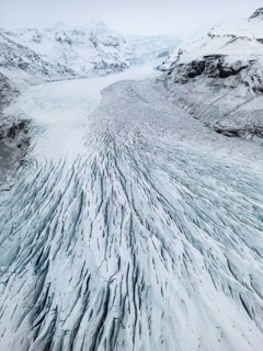 Aerial view of Icelandic winter landscape featuring a vast, icy glacier with intricate patterns.
