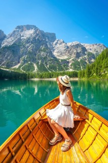 Woman wearing summer dress and hat enjoying boat trip on the alpine lake in dolomites mountains