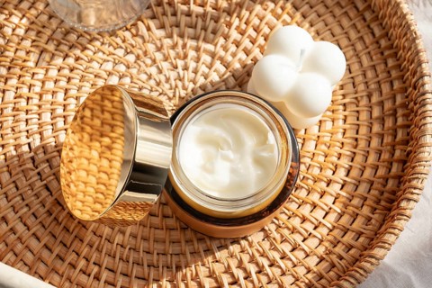 A luxurious skincare cream in an elegant gold jar, placed on a woven rattan tray beside a white