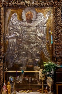 Archangel Michael, large angel statue in a gilded frame decorated with candles and flowers, Holy