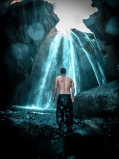 Adventurous young man under Gljufrafoss waterfall in winter in Iceland