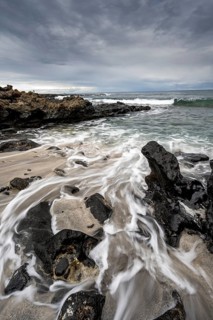 Waves blaze on the beach, rocky coast with volcanic stones, long exposure, Playa de la Pequeña,