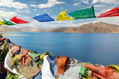 Colorful prayer flags flutter against the backdrop of the serene Pangong Tso lake, set amidst the