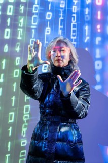 An elderly Asian woman with virtual reality glasses interacts in a digital metaverse environment.