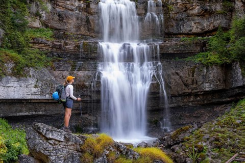 Young pretty hiker standing on rocks in front of Cascata di Mezzo waterfall, long exposure,