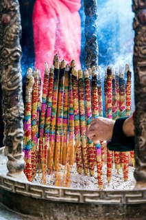 Cropped unrecognizable person holding a vibrant, large incense sticks burning, with smoke rising in