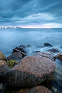 Rocks in the foreground lead to a bridge running across the sea in the distance, Öresund Bridge,