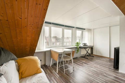 Spacious attic room featuring a slanted wooden ceiling, bright windows with a view, a cozy