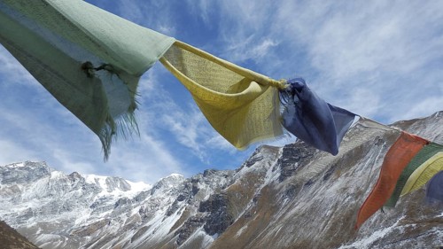 Various prayer flags flutter against snow-capped mountains in the background, trekking at Annapurna