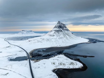 A breathtaking aerial view of Kirkjufell mountain in Iceland, covered in snow, surrounded by icy