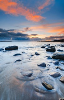 Orange coloured cloudy sky at sunset on a sandy beach strewn with round stones near Achiltibuie on