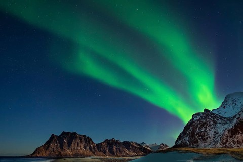 Aurora borealis in green colors over mountain range and coastline at night, Lofoten, Norway