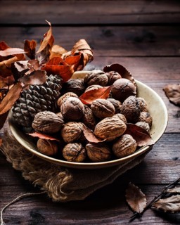 A cozy autumn still life featuring a bowl of walnuts, pine cone, and dried leaves on a rustic