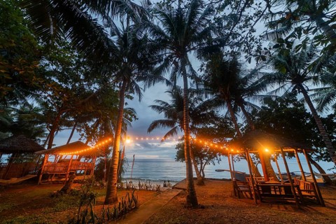 A serene beach view in the Philippines with bamboo huts lit by warm lights at twilight, showcasing