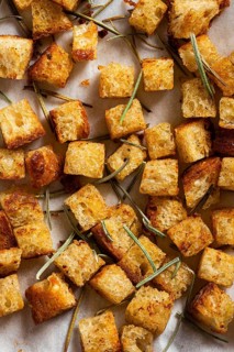 A close-up of golden croutons and rosemary, styled on a white background with tiles, capturing the