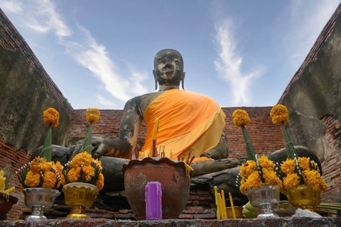 Majestic Buddha statue draped in orange cloth, surrounded by yellow flower offerings in Chiang Mai,