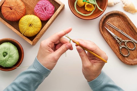 Top view of cropped unrecognizable hands of a woman crocheting in her studio. Surrounded by