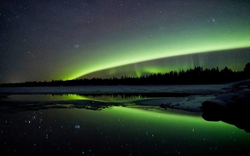 Aurora borealis in green colors over lake in snow covered landscape at night, Lapland, Finland