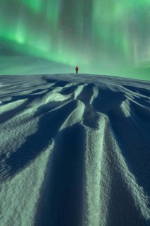 Unrecognizable person stands alone under the mesmerizing Aurora Borealis on a snowy landscape