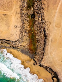 From above, an aerial shot captures a striking natural pool nestled within the rugged coastal