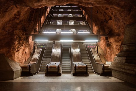 View of escalators at a Stockholm subway station, surrounded by cave-like rock formations. The