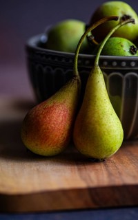 Close up of two wild pears resting on a wooden board with a decorative ceramic bowl filled with