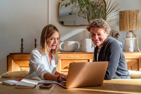 A couple works together at home, focused on a laptop The setting is cozy with a warm atmosphere,
