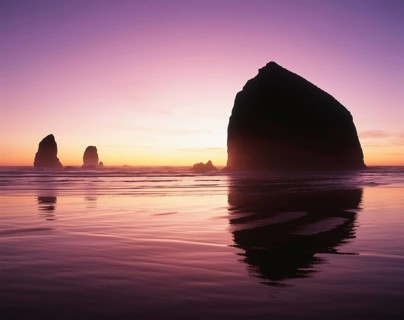 A serene sunset graces the horizon, illuminating ocean waters and silhouetting majestic rock