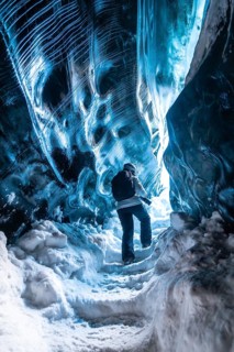 A person is walking through a cave with blue walls. The cave is very cold and the person is wearing