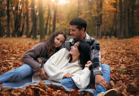 A joyful family relaxes in a forest amidst colorful autumn leaves. The warm tones and soft light