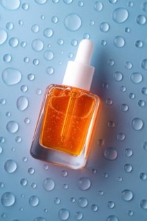 A bottle of vitamin C serum with a pipette, filled with vibrant orange liquid, is set against a