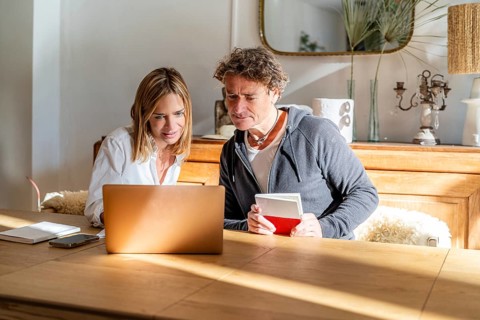 A couple working together at home, engaged with their laptop and notes Sunlight fills the cozy
