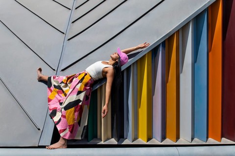 A woman in a vibrant, colorful outfit contrasts strikingly with modern architectural design,