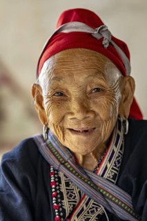 Portrait of an elderly woman with a traditional headscarf and smiling face, large Buddha statue at