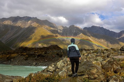 A woman stands on rocky terrain, admiring a vibrant autumn landscape on Mount Cook, New Zealand,