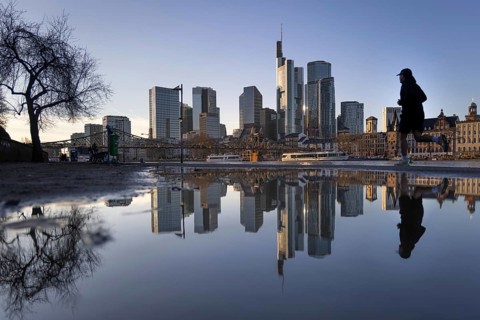 Frankfurt's banking skyline and a jogger running by are reflected in a puddle on the banks of the