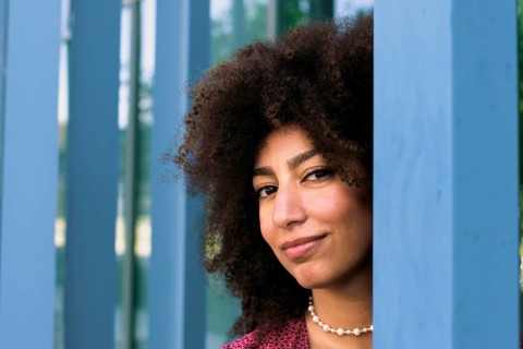 A young Arab woman with curly hair smiles confidently looking at camera, framed by blue columns.
