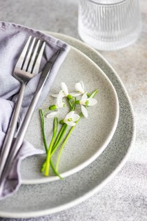 Textured grey plate featuring fresh spring snowdrops alongside a fork and a soft cloth napkin,