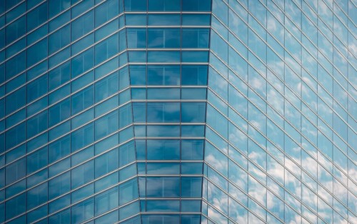 Close-up of a modern glass building facade reflecting a clear blue sky and fluffy clouds,