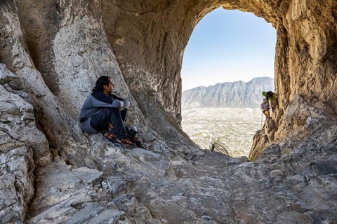 A climber rests on rocky terrain while two others practice mountaineering and rappelling in