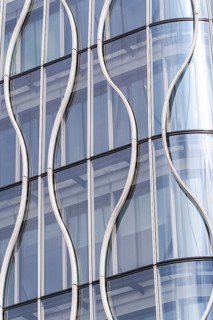 Close-up of a modern building facade, showcasing wavy glass panels and sleek metal frames. The