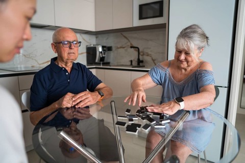 A multigenerational family gathers around a kitchen table, enjoying a lively game of dominoes.