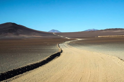A desolate yet striking view of a dirt road meandering through the arid terrain of La Puna in