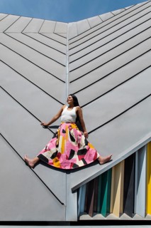 A woman wearing a vibrant, colorful outfit poses against striking modern architecture, showcasing a