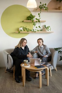 Two women engage in a business meeting at a cozy cafe. They are discussing something on a tablet,