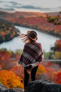 A woman in a hat and plaid shawl stands overlooking a picturesque Quebec landscape in autumn. The