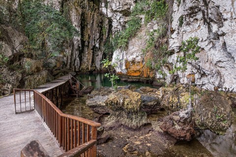 A scenic boardwalk winds through a cave, surrounded by lush foliage and rocky terrain in Indonesia.