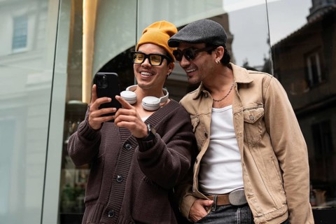 A joyful gay couple shares a moment of laughter while looking at a smartphone. They stand together